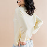 Woman wearing a light-colored sweater and jeans against a beige background