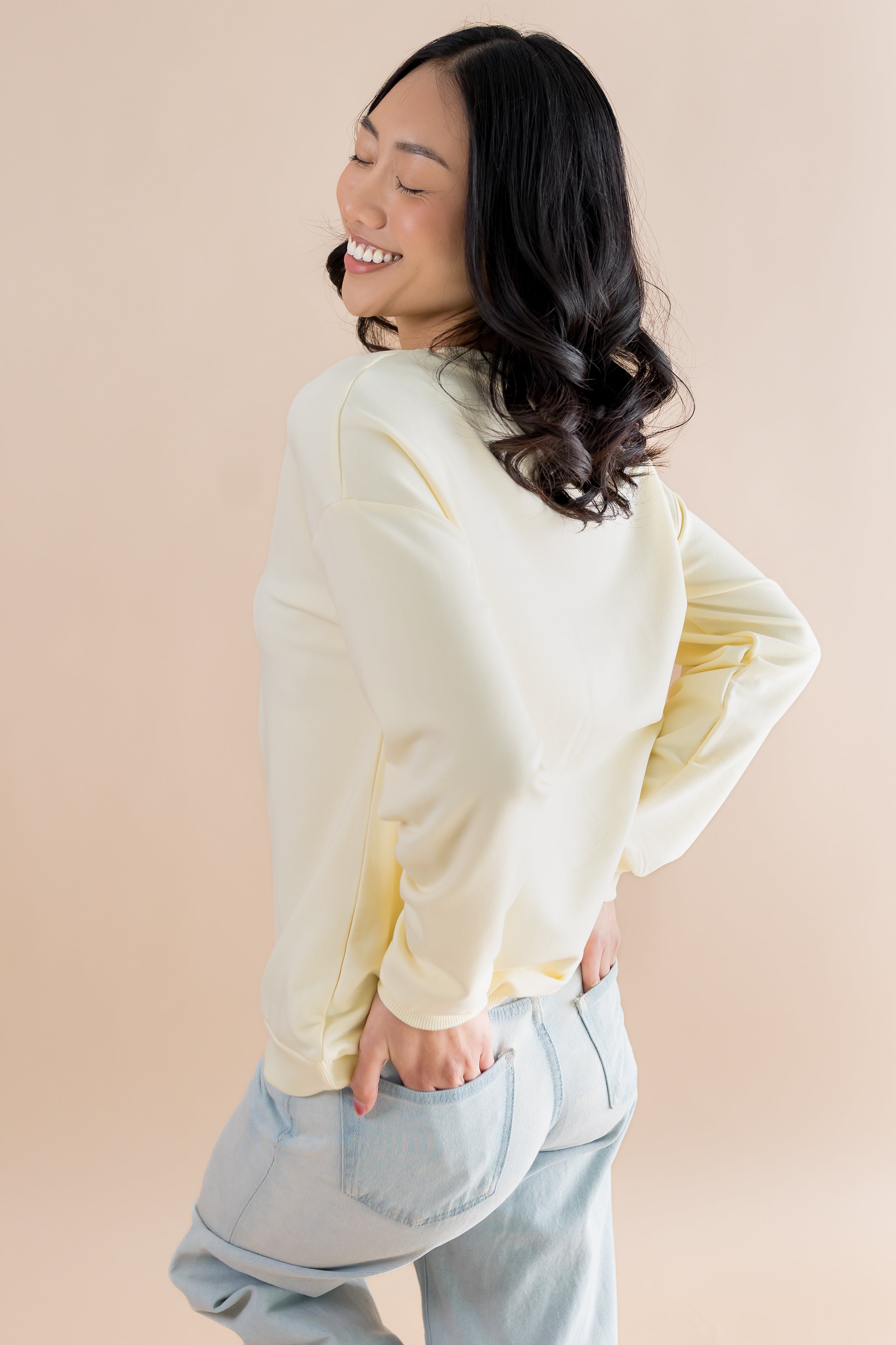 Woman wearing a light-colored sweater and jeans against a beige background