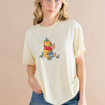Woman wearing a yellow-colored t-shirt with a Winnie the Pooh character on a beige background ::: Model is 5'7" wearing size S ///