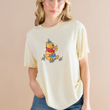 Woman wearing a yellow-colored t-shirt with a Winnie the Pooh character on a beige background ::: Model is 5'7" wearing size S ///