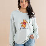 Woman wearing a light blue sweatshirt with a cartoon character design on a beige background ::: Model is 5' wearing size XS ///