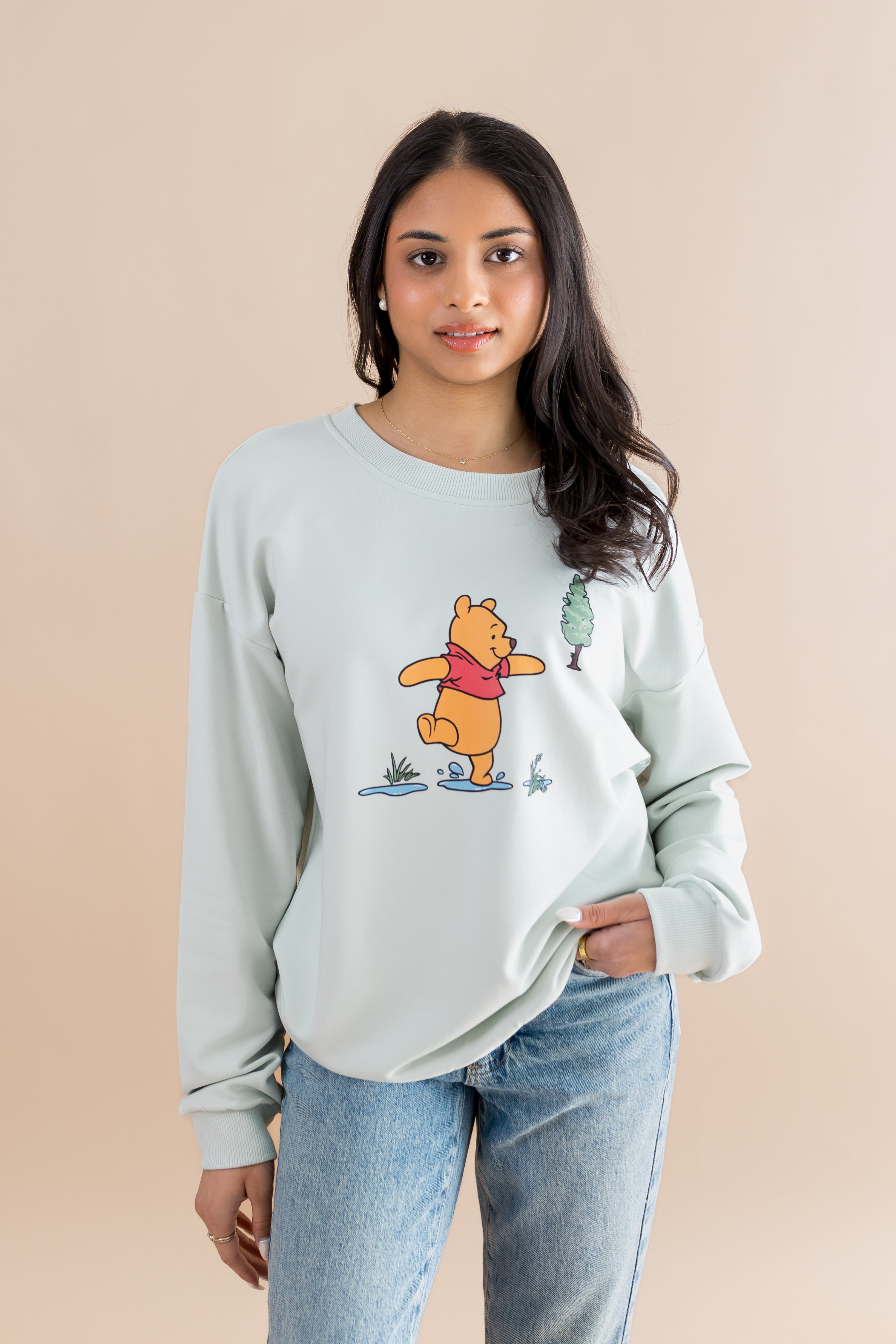 Woman wearing a light blue sweatshirt with a cartoon character design on a beige background 