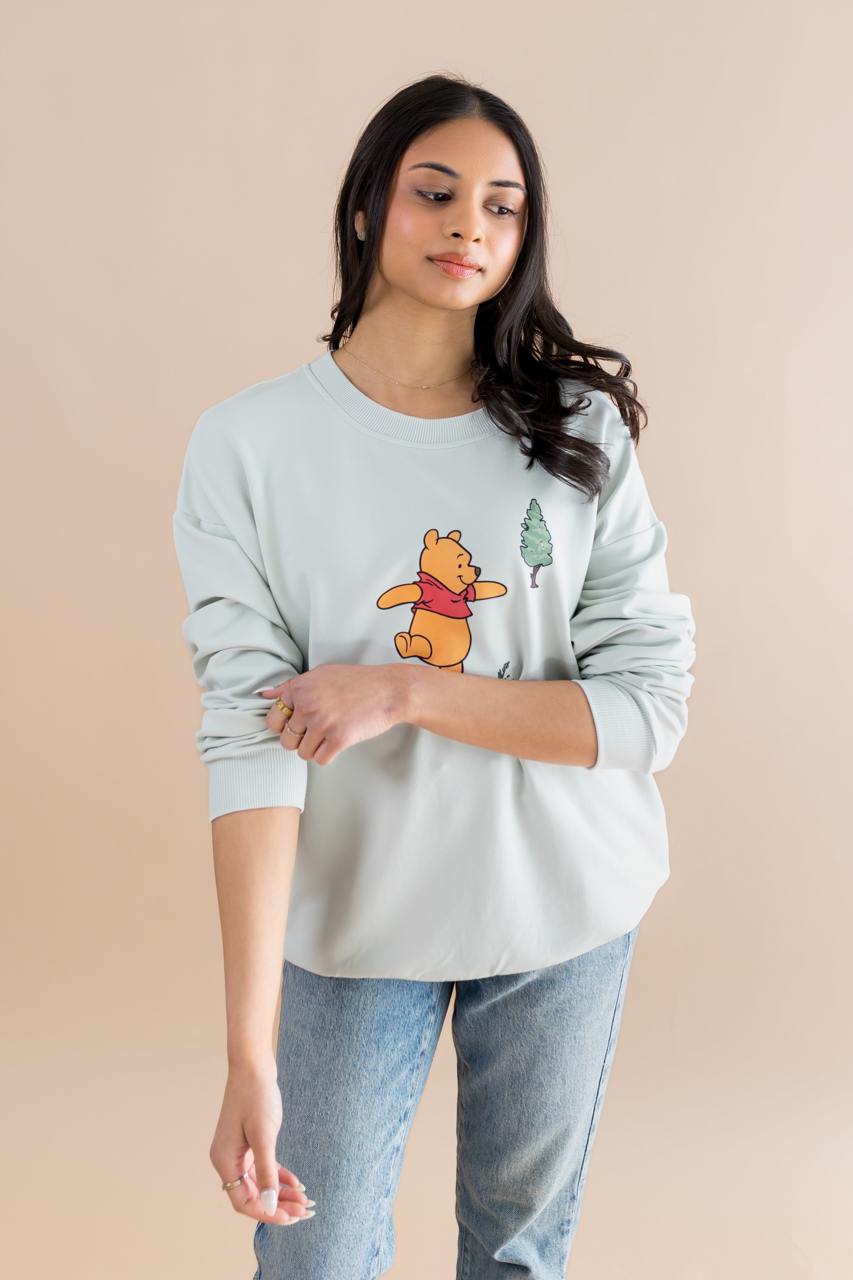 Woman wearing a light blue sweatshirt with a cartoon character on a beige background