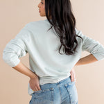 Woman wearing a light blue sweater and blue jeans against a beige background