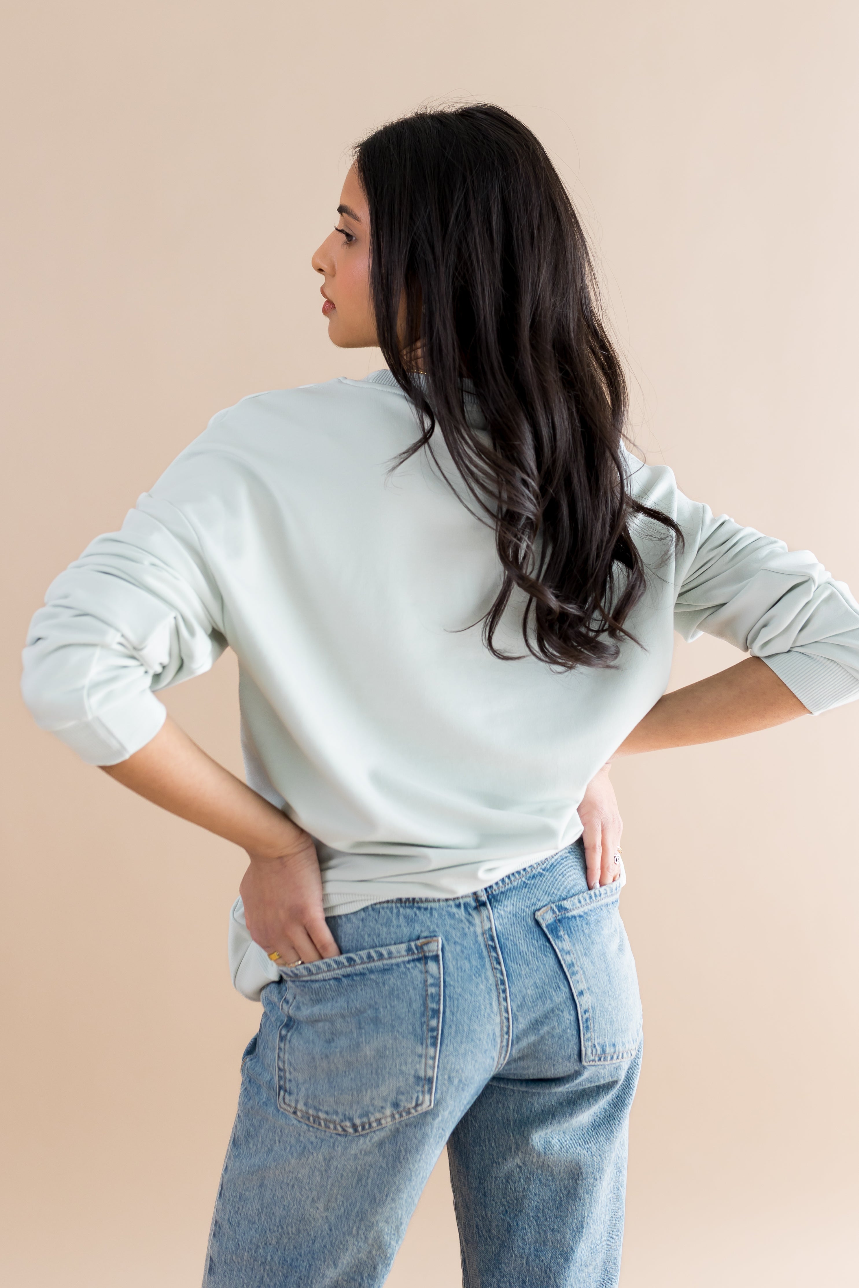 Woman wearing a light blue sweater and blue jeans against a beige background