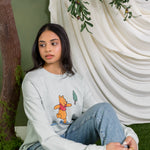 Women in light blue sweatshirt with Winnie the Pooh forest graphic sitting in a forest studio setting ::: Model is 5' wearing size XS ///