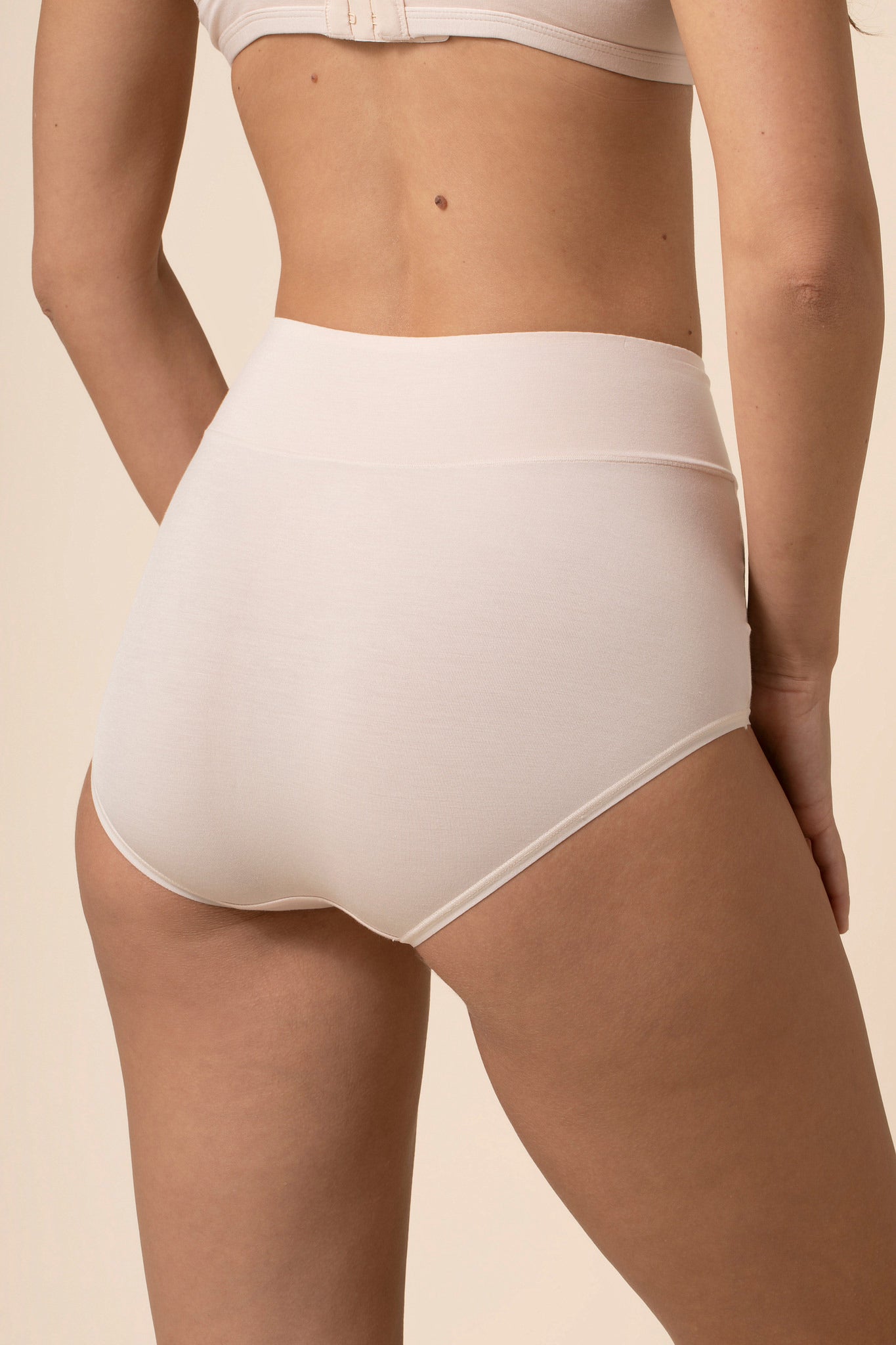Person wearing cream high-waisted underwear on a beige background