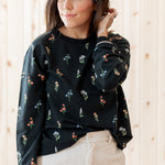 Model standing in front of a light birch back ground while modeling the Women's Sweatshirt in Midnight Wildflower paired with light bottoms
::: Model is 5'3" wearing size S ///