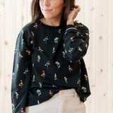 Model standing in front of a light birch back ground while modeling the Women's Sweatshirt in Midnight Wildflower paired with light bottoms
::: Model is 5'3" wearing size S ///