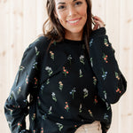 Smiling model wearing the Women's Sweatshirt in Midnight Wildflower paired with a light paired bottoms