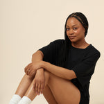 Model posing with knees up and arms crossed over knees while wearing the Women's Boxer in Midnight paired with the Women's Tee in Midnight 