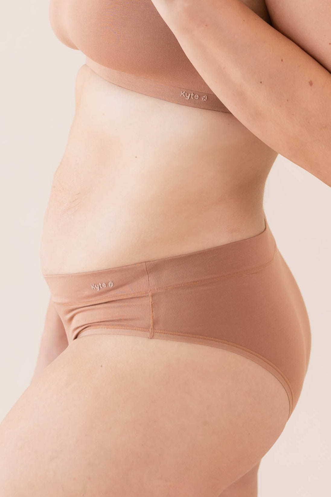 Brown cheeky underwear worn by a person on a light pink background