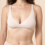 Woman wearing a beige cross front bra and underwear set against a beige background