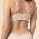Woman wearing a beige bra and underwear set against a beige background