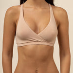 Woman wearing a beige cross over bra and panties set against a neutral background