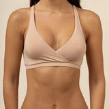 Woman wearing a beige cross over bra and panties set against a neutral background