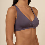 Woman wearing a dark purple cross over bra against a beige background