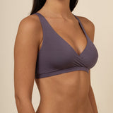 Woman wearing a dark purple cross over bra against a beige background