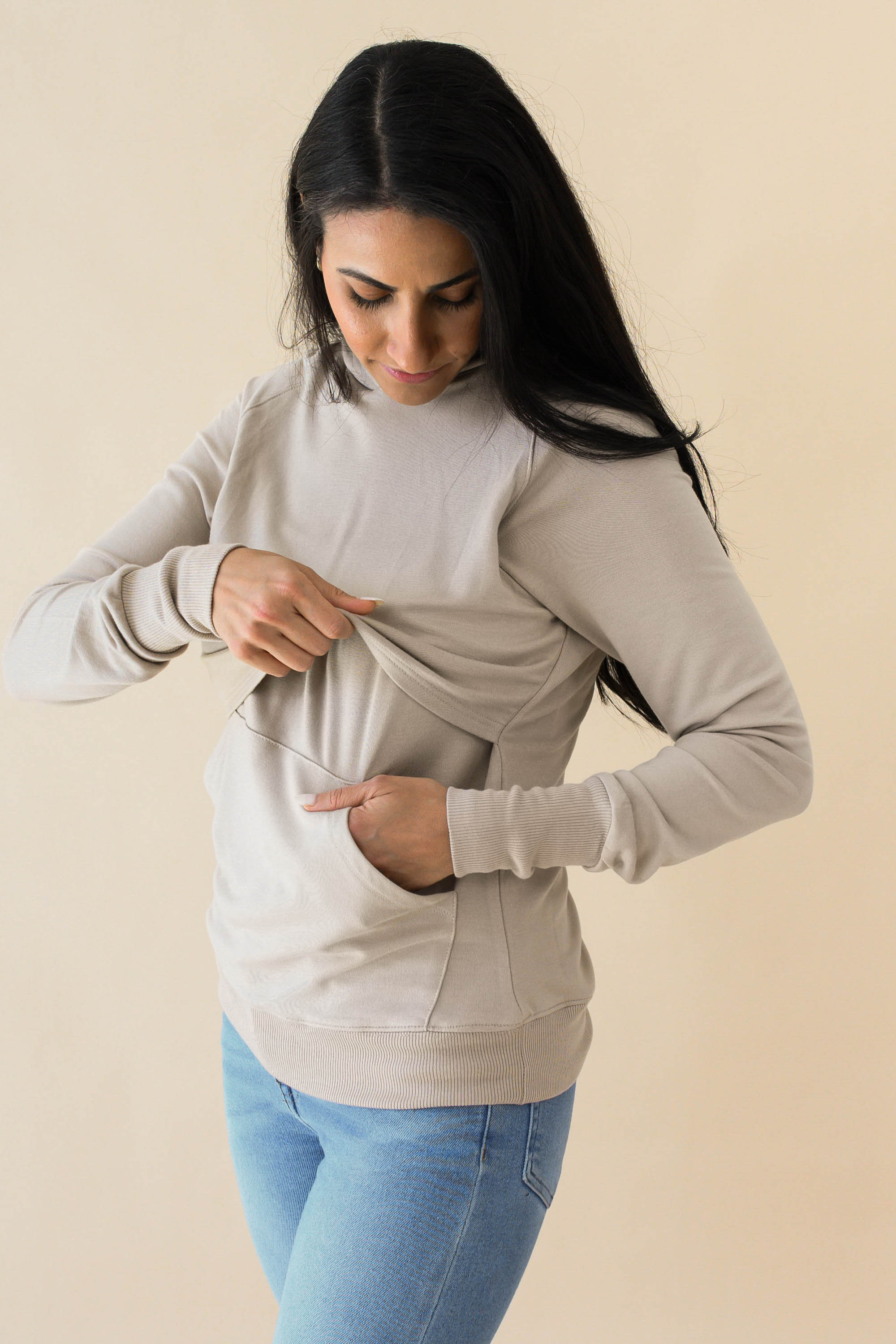 Female model lifting up the front of the Women's French Terry Nursing Hoodie in Almond while other hand is in pocket
