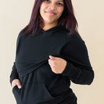 Model lifting up the front fabric of the hoodie showing the functionality for breastfeeding for the Women's French Terry Nursing Hoodie in Midnight