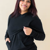 Model lifting up the front fabric of the hoodie showing the functionality for breastfeeding for the Women's French Terry Nursing Hoodie in Midnight