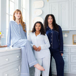 Three women in blue pajamas sitting on a window sill in a light blue room.