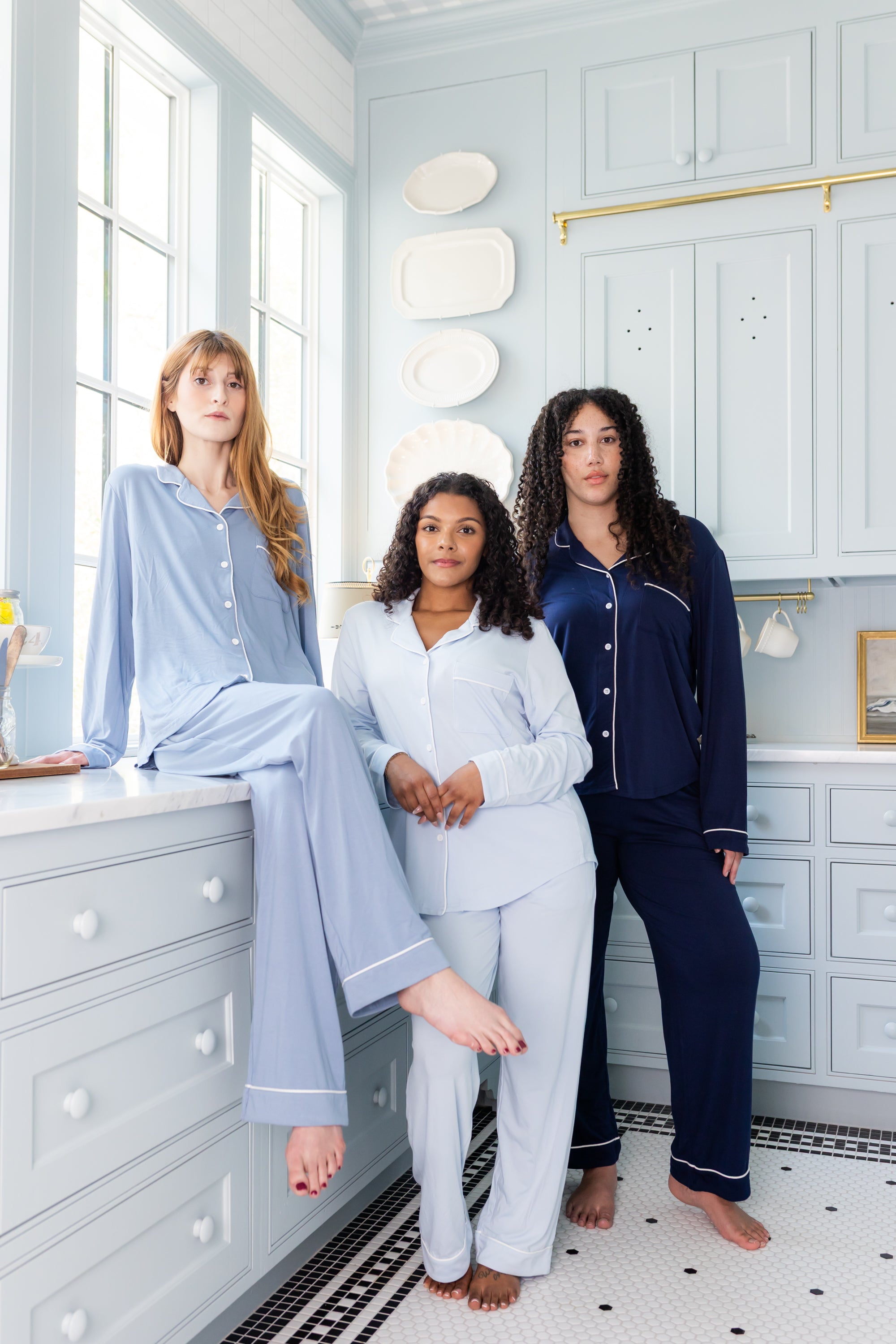 Three women in blue pajamas sitting on a window sill in a light blue room.