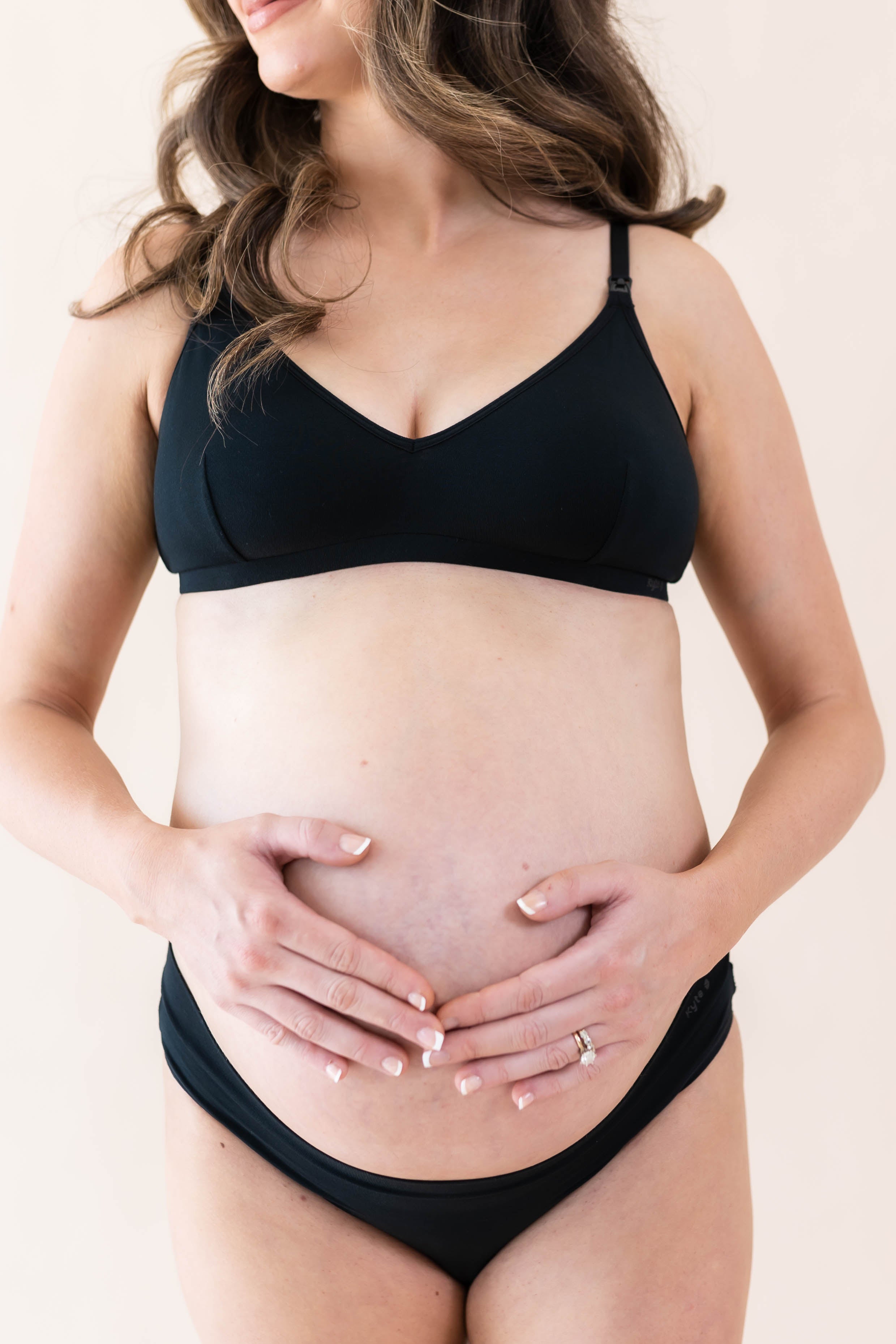Expectant mother with hands on stomach wearing Kyte Baby's Women's Nursing Bra in Midnight