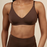 Woman wearing a brown nursing bra and high-waisted leggings against a beige background