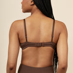 Woman wearing a brown nursing bra and pants against a beige background
