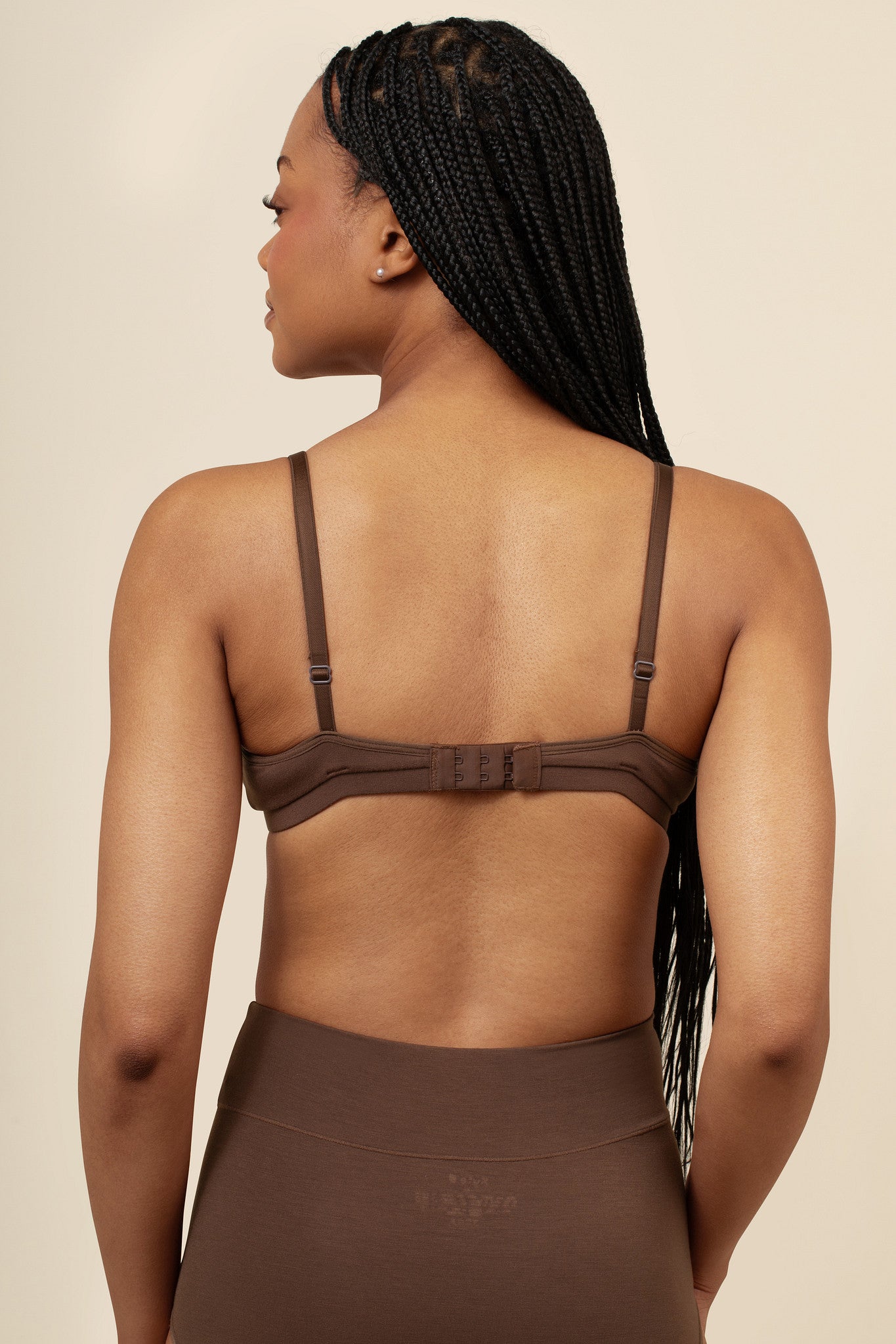 Woman wearing a brown nursing bra and pants against a beige background