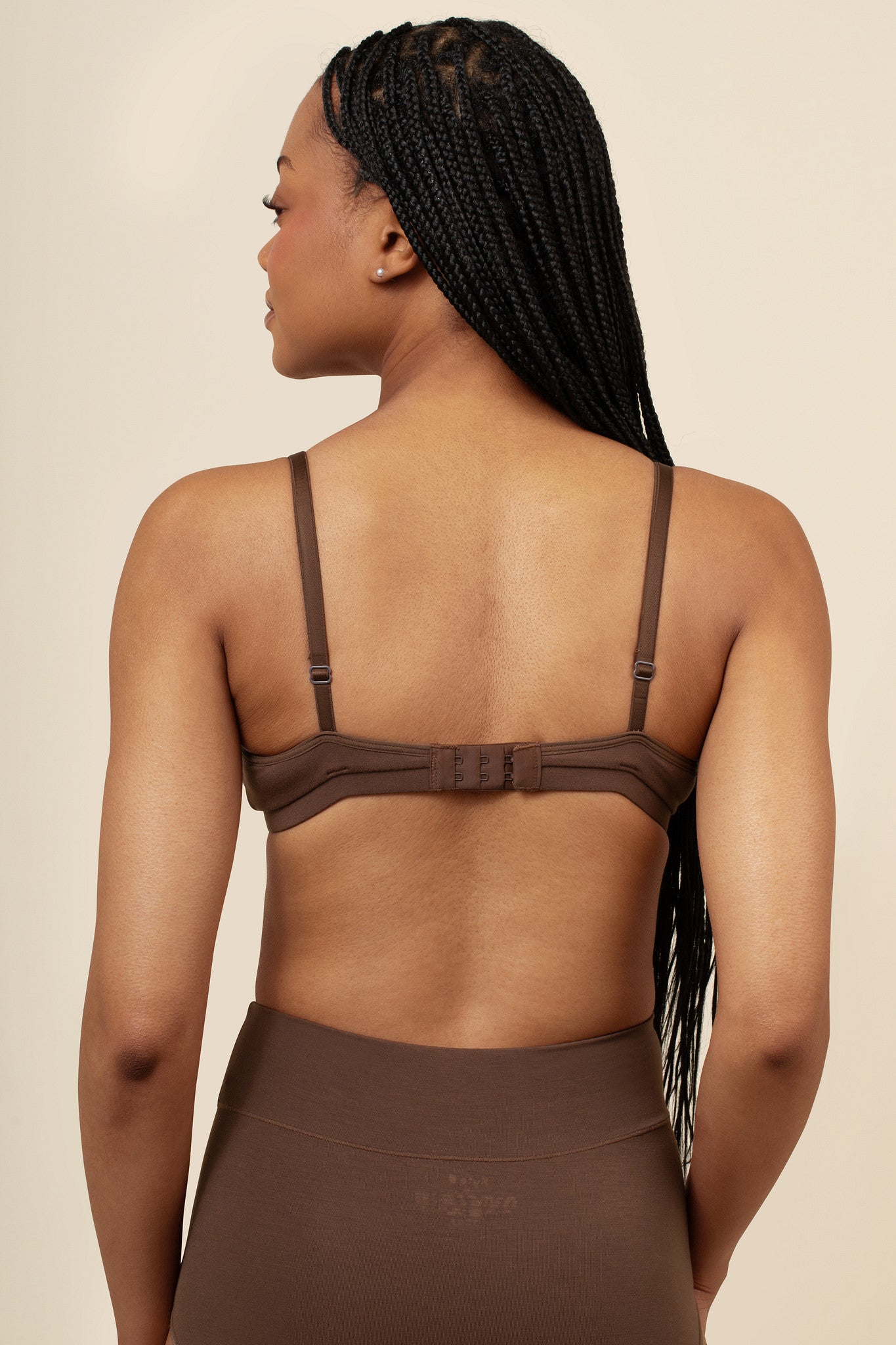 Woman wearing a brown nursing bra and pants against a beige background