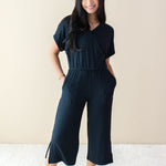 Female model wearing the Women's Ribbed Jumpsuit in Midnight with both hands in pockets