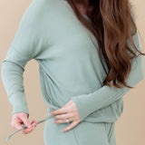 Model showing the drawstring feature for cinching on the bottom of the shirt for the Women's Ribbed Long Sleeve Drop Shoulder Top in Thyme