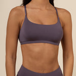 Person wearing a dark purple scoop bra and leggings on a beige background