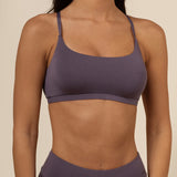 Person wearing a dark purple scoop bra and leggings on a beige background