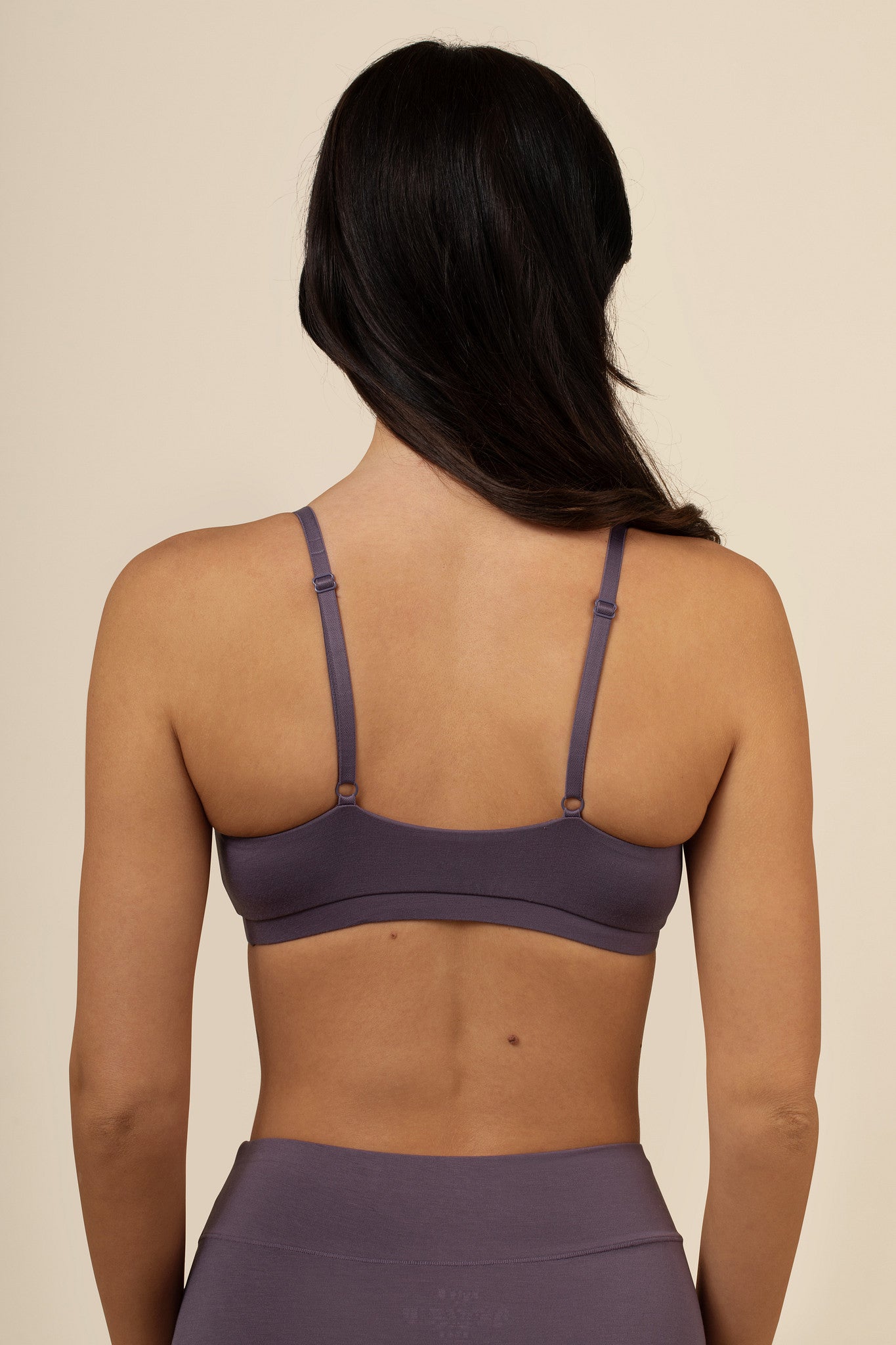 Woman wearing a purple bra and leggings on a beige background