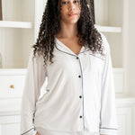Woman wearing white pajamas with black trim in a room with shelves.