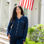 Woman wearing a navy blue pajama set standing in front of a house with an American flag.