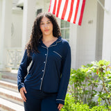 Woman wearing a navy blue pajama set standing in front of a house with an American flag.