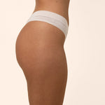 Light cream colored thong worn by a person on a beige background showing side coverage