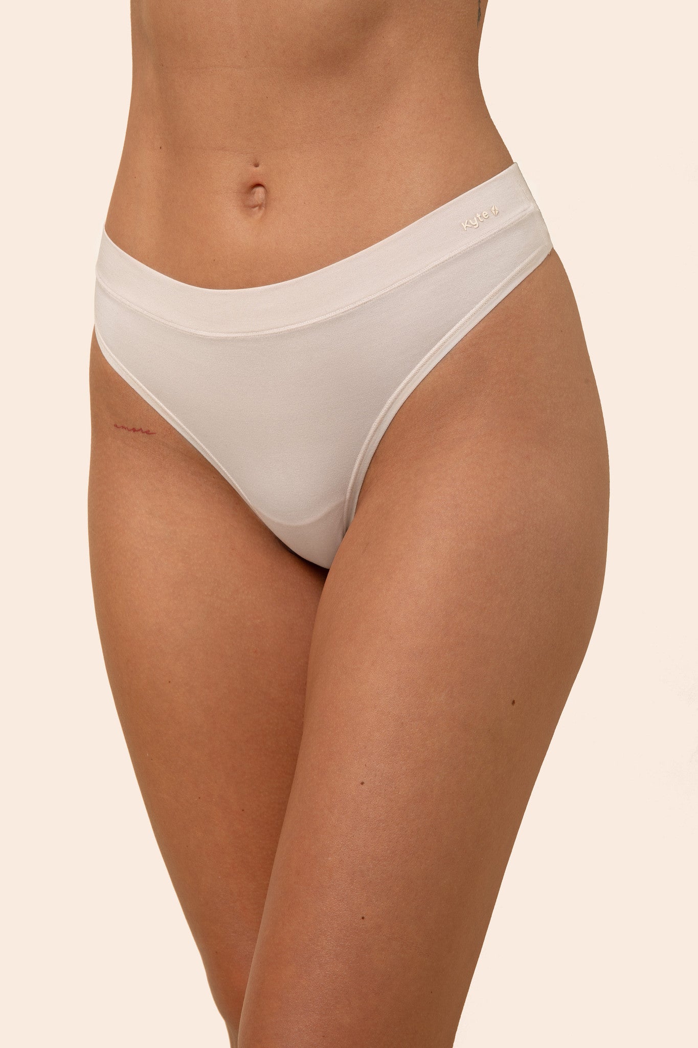 Light cream colored thong worn by a person on a beige background