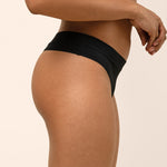 Black thong worn by a person on a beige background showing side coverage
