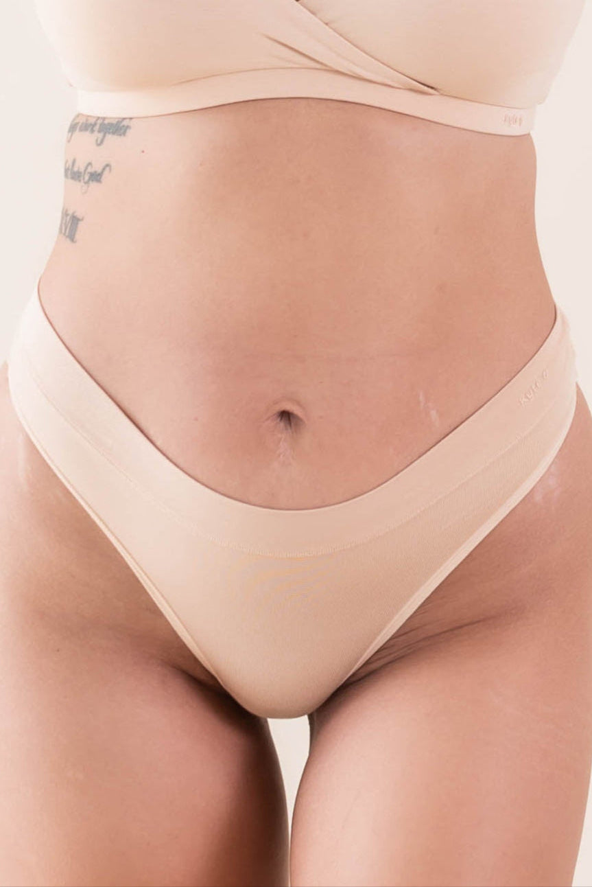 Woman wearing matching thong and bralette in a light tan color