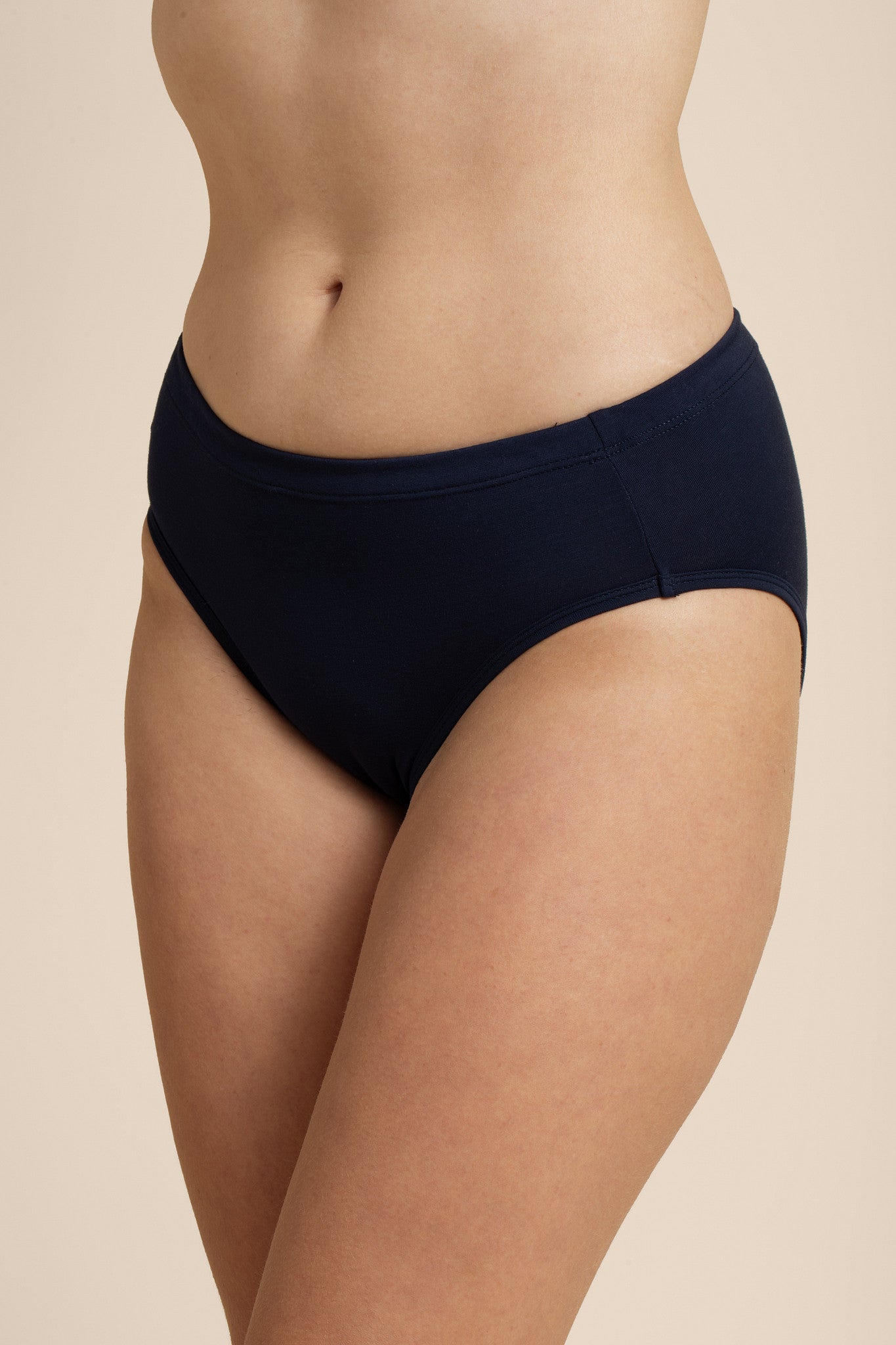 Person wearing a navy mid-waisted bikini bottom on a beige background