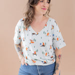 Woman wearing a light-colored blouse with cartoon character print and blue jeans against a beige background