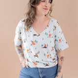 Woman wearing a light-colored blouse with cartoon character print and blue jeans against a beige background