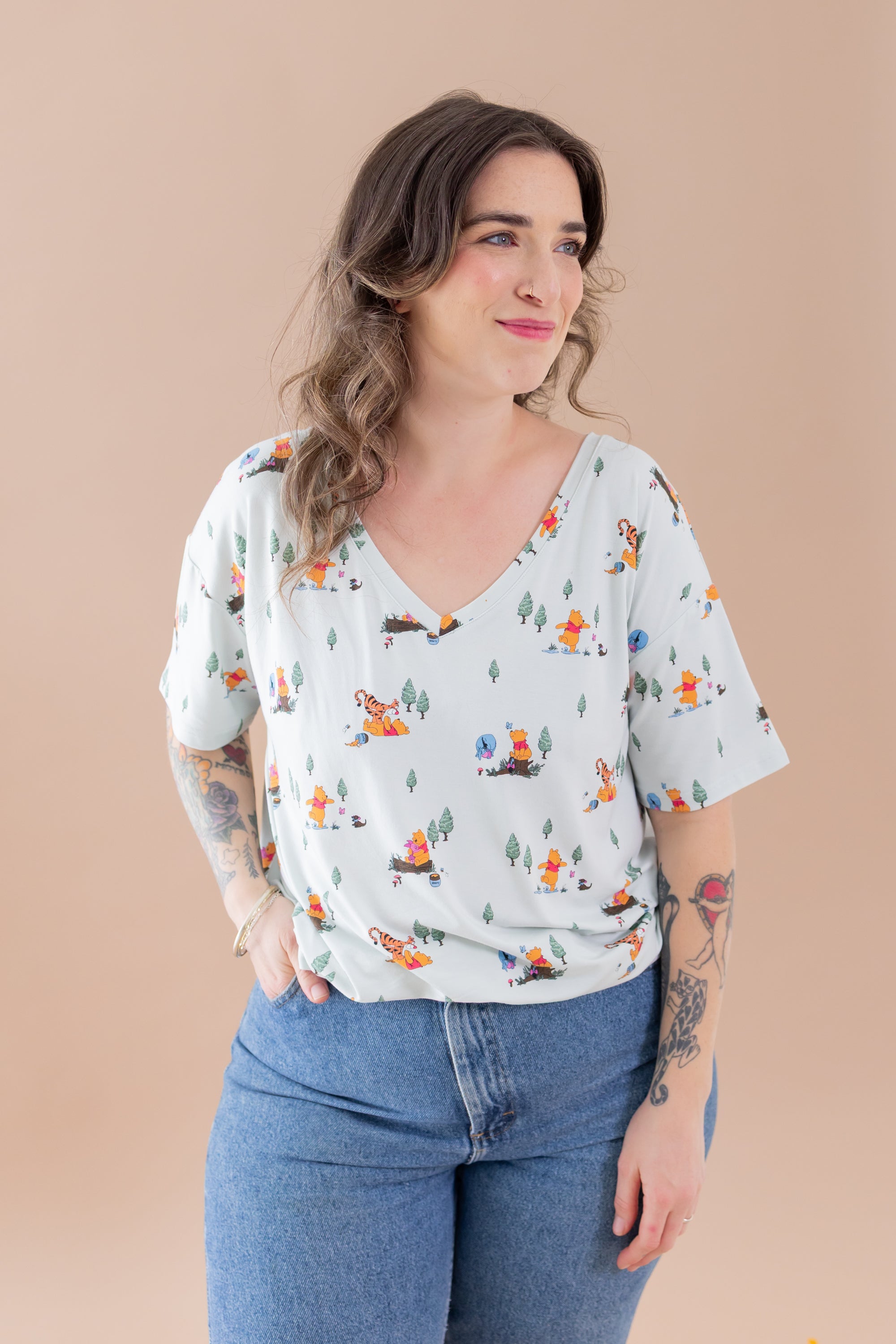 Woman wearing a light-colored blouse with cartoon character print and blue jeans against a beige background