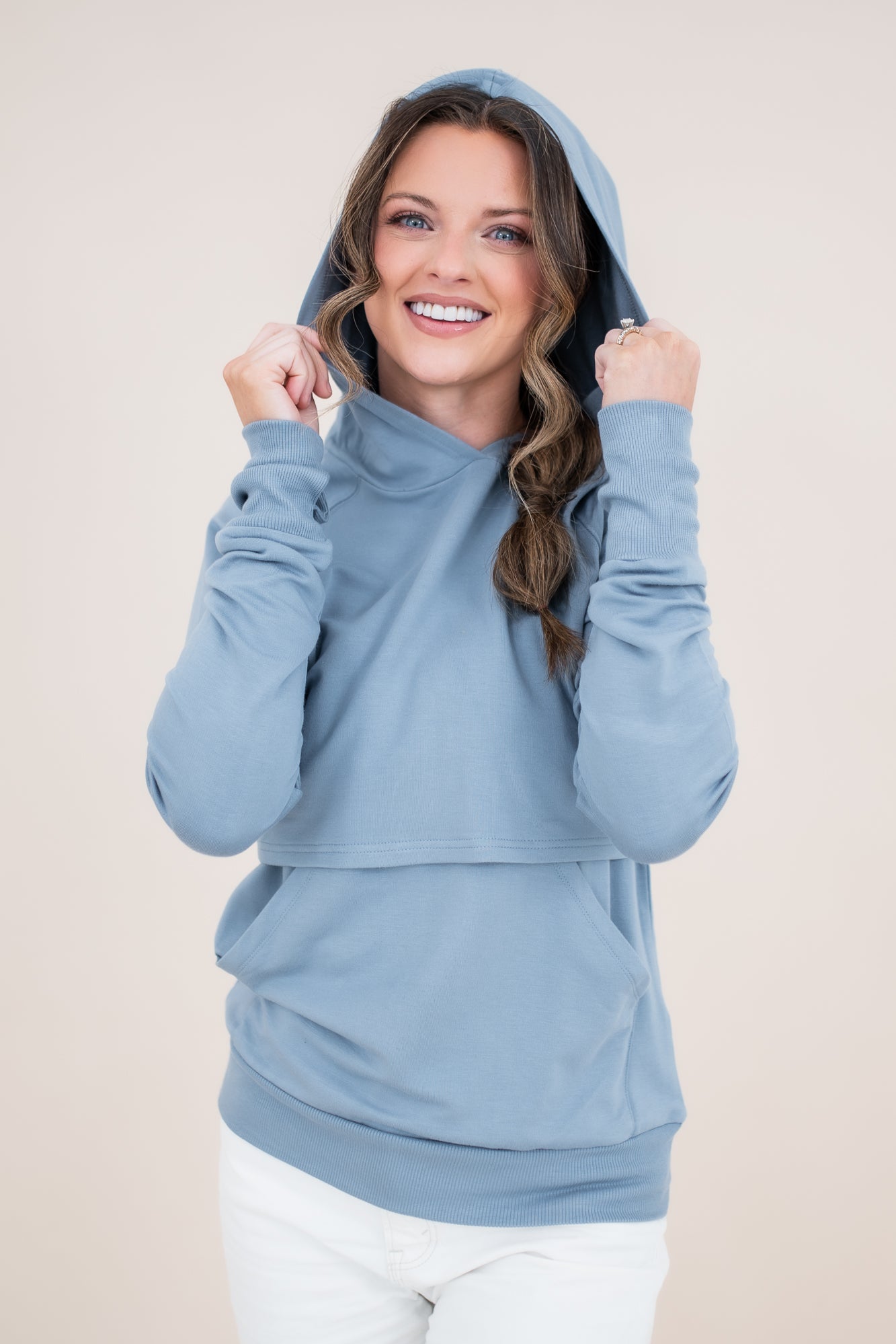Smiling model wearing the Women's French Terry Nursing Hoodie in Slate with the hoodie up and her hands on the hood