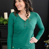 Model looking to the side with her hand on her hip while wearing the Women's Long Sleeve Henley Tee in Emerald